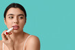 © Pixel-Shot - Young woman applying lip balm on color background