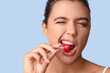 © Pixel-Shot - Young woman with beautiful lips eating lollipop on blue background, closeup