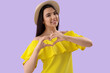 © Pixel-Shot - Young woman making heart with her hands on lilac background