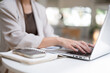 © bongkarn - Close up of a woman's hand wearing rings typing on laptop beside notebook while sitting in the cafe.
