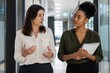 © momostudio - Two professional women engaged in conversation in a modern office setting.