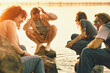 © master1305 - Laughing friends crouching by lakeshore at sunset with nostalgic film grain. Concept of candid youth content, friendship campaigns, summer fun, travel memories, and emotional lifestyle ads.