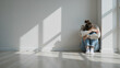 © thiraphut - A lonely woman sits curled up on a wooden floor in the corner of a bright, minimalist white room with dramatic window shadows, evoking feelings of depression, anxiety, and isolation.