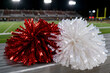 © Мария Ковалева - Red and white cheerleading pompoms lying on stadium bench at night, close-up with football field background
