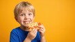 © Taras Roshchuk - A boy holds a slice of pizza with cheese in one hand and smiles widely. He has short blonde hair and wears a blue shirt. The bright yellow background draws attention to him eating