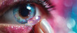 © Alexandra - Close-up of a person placing a contact lens on their eye, with vibrant pink and blue background and sparkling makeup.