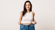 © Bayu Tri Nugroho - Happy young woman smiling proudly holding out oversized jeans to showcase weight loss or clothing fit achievement in a bright minimal studio setting
