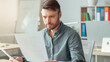 © Prostock-studio - Focused Caucasian Male Professional In His 30s Reading Documents At Modern Office Workspace, Sitting At Desk With Laptop And Papers, Engaged In Work. Business Concept
