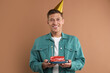 © New Africa - Man holding piece of cake with burning candle on pale brown background