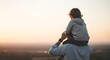 © Mumu - Rear view of a father carrying his young son on his shoulders during a beautiful sunset, looking out over a blurred landscape horizon with soft golden hour lighting and warm tones.