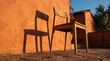 © Dowidodo - Wooden chair casting a long shadow on a terracotta wall in sunlight
