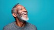 © MarkelovaVision - Happy senior Black man laughing with joy against a vibrant teal background.