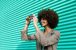 © VISTA by Westend61 - Cheerful woman with afro taking photo against turquoise wall