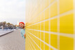 © VISTA by Westend61 - Smiling face peeking behind a bright yellow wall in Barcelona
