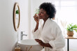 © Westend61 - Smiling woman massaging face looking in mirror at home