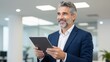 © junet - Smiling businessman using tablet in modern office setting technology