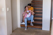 © wavebreak3 - Two men sitting on wooden open-tread staircase at home, embracing with wristwatch and sneakers