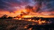 © Cleverson - Prairie fire rages across dry grass field at sunset with dramatic clouds and distant farm buildings