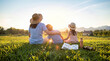 © 沈军 贡 - A mother and two children sit closely on a lush green meadow, enjoying the warm sunset view over the rural countryside landscape.