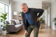 © Meow Creations - Concerned senior man holding his lower back and knee while wincing slightly in pain