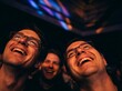 © kiwir - Three happy men laughing together looking up in awe at a concert or event with colorful lights shining down