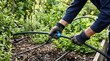© AynunNaher - Gardener connecting black irrigation drip line tubing in garden soil for efficient watering.