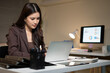 © Stella 16 - Asian Businesswoman Working Late at Night on Laptop in Modern Office with Data Charts on Monitor