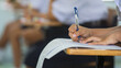 © arrowsmith2 - Close-up of a student's hand diligently writing on an exam paper during a school test. The student is using a professional pen , sitting at a wooden desk in a brightly lit classroom.