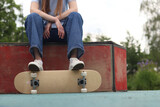 Legs of skateboarder in white sneakers and baggy jeans standing on skateboard in skate park. Concept of street style, youth culture and outdoor activities. Young girl resting with skateboard