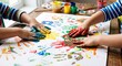 © Natalia - Close-up photo of children creating colorful handprints with bright paint on large paper at a table, expressing creativity, teamwork, early learning, fun education and playful development.