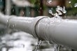 © Kristina - Water flows from a broken pipe in a garden during daylight hours creating splashes and puddles on the ground