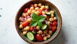 © Maryna - Close up of chickpea salad bowl with tomatoes, cucumbers, and red onion. Fresh green parsley leaf garnishes dish. Healthy plant based meal on white surface.