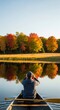 © Margarita Ratatosk - Man paddling canoe on calm lake in autumn season observing colorful fall trees reflected on water. Nature exploration and tranquil outdoor activity concept.