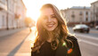 © Fresh - Smiling young woman with wavy hair in soft sunlight on a city street, golden hour glow, positive mood