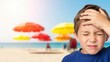 © Audax - Young boy holding head with pain on bright sunny beach.