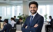 © Kevin - Smiling indian man with a beard, wearing a dark suit and blue tie, poses with his arms crossed in a modern office environment.