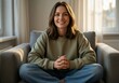 © KarpenArt Studio - Smiling woman in casual attire sitting comfortably on a gray sofa in a softly lit home interior.