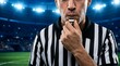 © Pixels Stock - Sports referee blowing whistle in close up view, stadium background with bright lights and blurred audience during evening match.