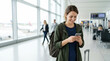 © Xenia - Young woman using smartphone at airport terminal. Traveler waiting for flight with luggage. Travel concept