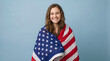 © Achraf - Teenage girl wrapped in American flag on soft blue background, patriotic 4th of July portrait celebrating Independence Day, freedom, liberty and national pride in USA
