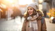 © gedang - Smiling young woman in warm winter clothes and knitted hat walking on a sunny city street, golden hour lighting