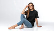 © Kaizostock921 - Young woman with curly hair wearing glasses and casual outfit sitting on floor, looking at camera