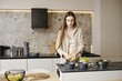 © Aleksei Isachenko/imageBROKER - A pregnant woman stands in a stylish kitchen, chopping vegetables. She wears a casual outfit and showcases a serene demeanor. The sunlight enhances the contemporary decor and creates a warm ambiance