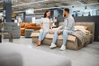 © Serhii - Young couple sitting on bed in furniture store