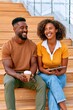 © Georgii - Smiling young couple sitting on wooden stairs enjoying coffee and tablet in a casual urban setting