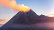 © AmazingAerialAgency - Aerial view of an active volcano with a thick plume of smoke rising from the crater during golden hour with mist at the base in Indonesia.