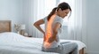 © Zampra studio's  - A young woman sitting on the edge of a bed grimacing in severe lower back pain, with a glowing red holographic overlay highlighting a damaged spine.