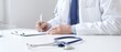 © rogerphoto - Closeup of blue stethoscope is lying on the table near doctor man professional writing on the clipboard in clinic office. Medicine and healthcare