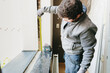 © Nataliya - A portrait of an adult master takes measurements of a window opening in a room with a tape measure.