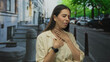 © Krakenimages.com - Young woman clutching throat and chest on street beside stone steps and parked cars; distress health concern.